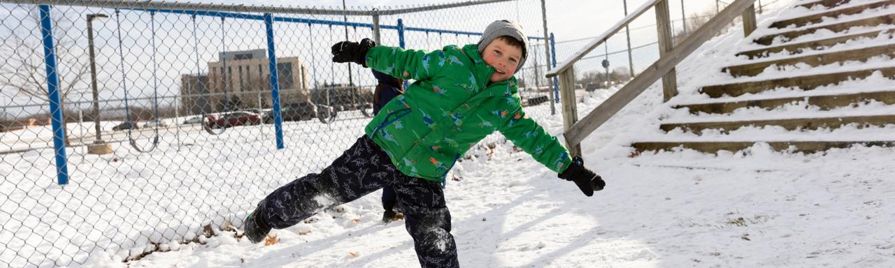 Kid standing on one leg with arms out in the snow
